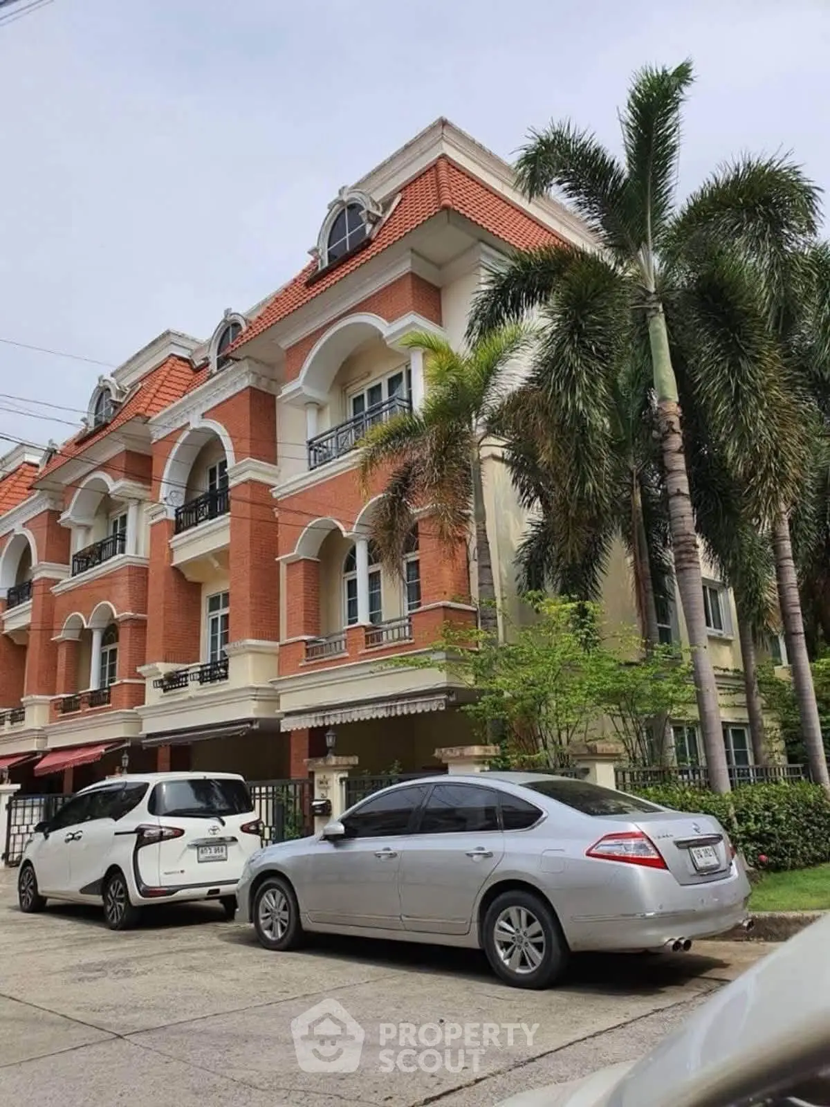 Elegant multi-story brick building with arched windows and palm trees, featuring parked cars in a serene neighborhood.