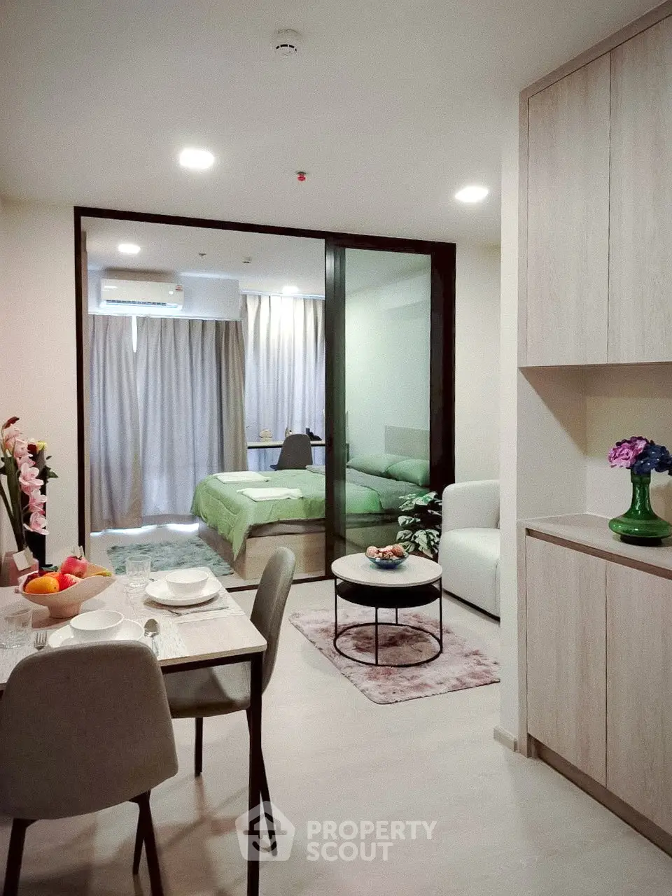 Modern studio apartment with open layout, featuring a cozy living area and stylish bedroom separated by glass doors.