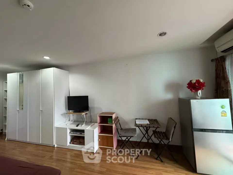 Spacious studio apartment with modern furnishings and wooden flooring, featuring a cozy seating area and ample storage.