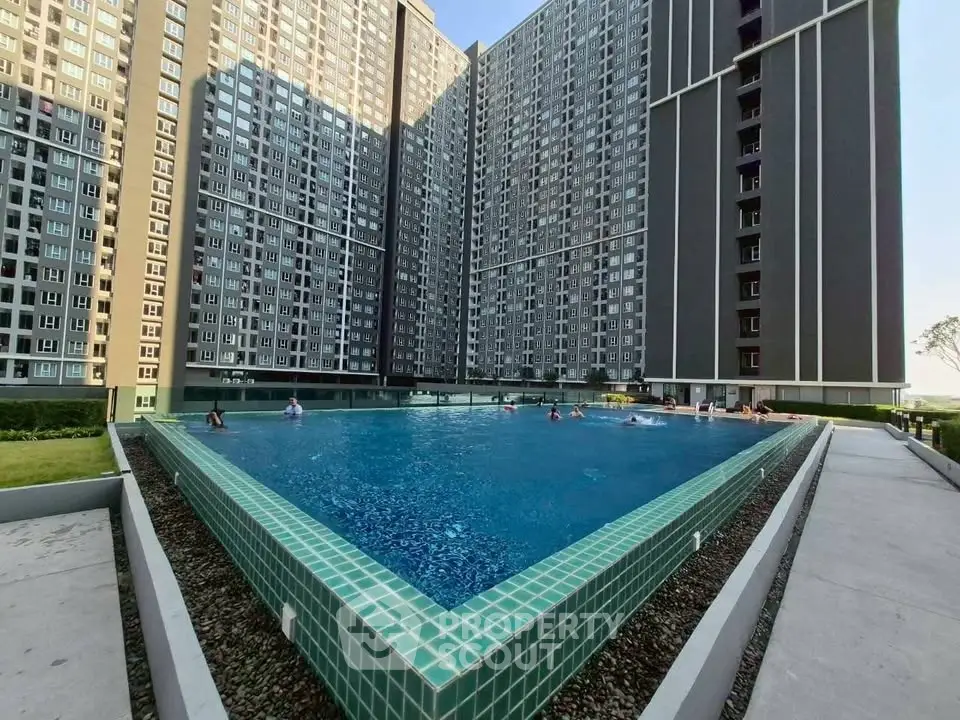 Modern high-rise apartment complex with large outdoor swimming pool and lush greenery.