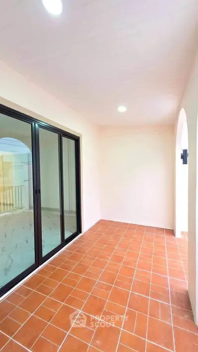 Spacious balcony with terracotta tiles and sliding glass doors in modern apartment.