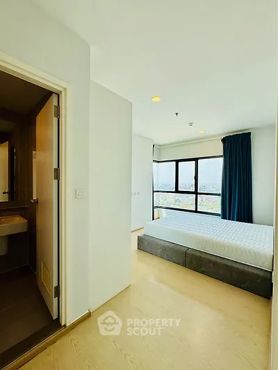 Bright bedroom with large window offering stunning city view, adjacent to modern bathroom.