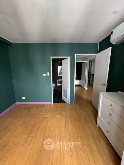 Spacious room with wooden flooring and green walls, featuring a dresser and air conditioning.