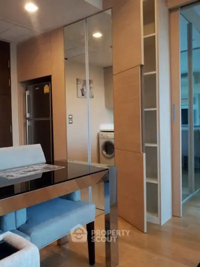 Modern apartment interior with dining area and washing machine, featuring sleek wooden cabinetry.