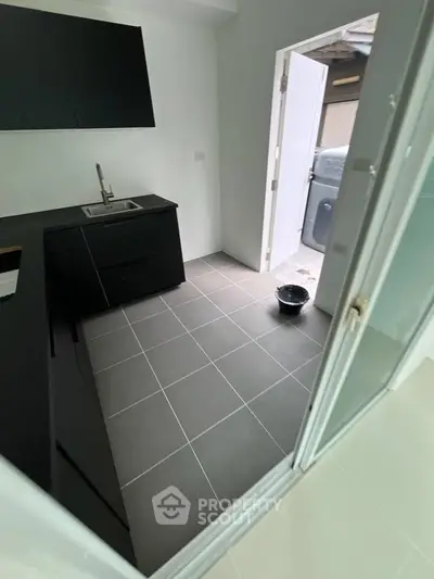 Modern kitchen with sleek black cabinetry and open layout leading to outdoor area.