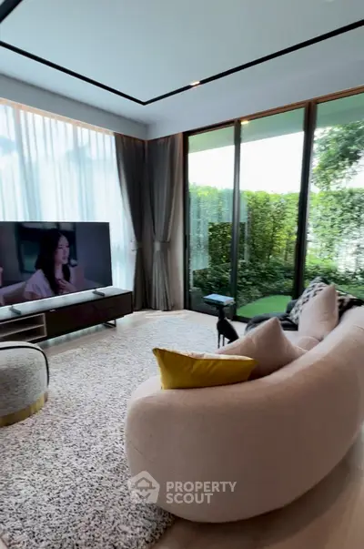 Luxurious living room with modern sofa, large TV, and garden view through glass doors.