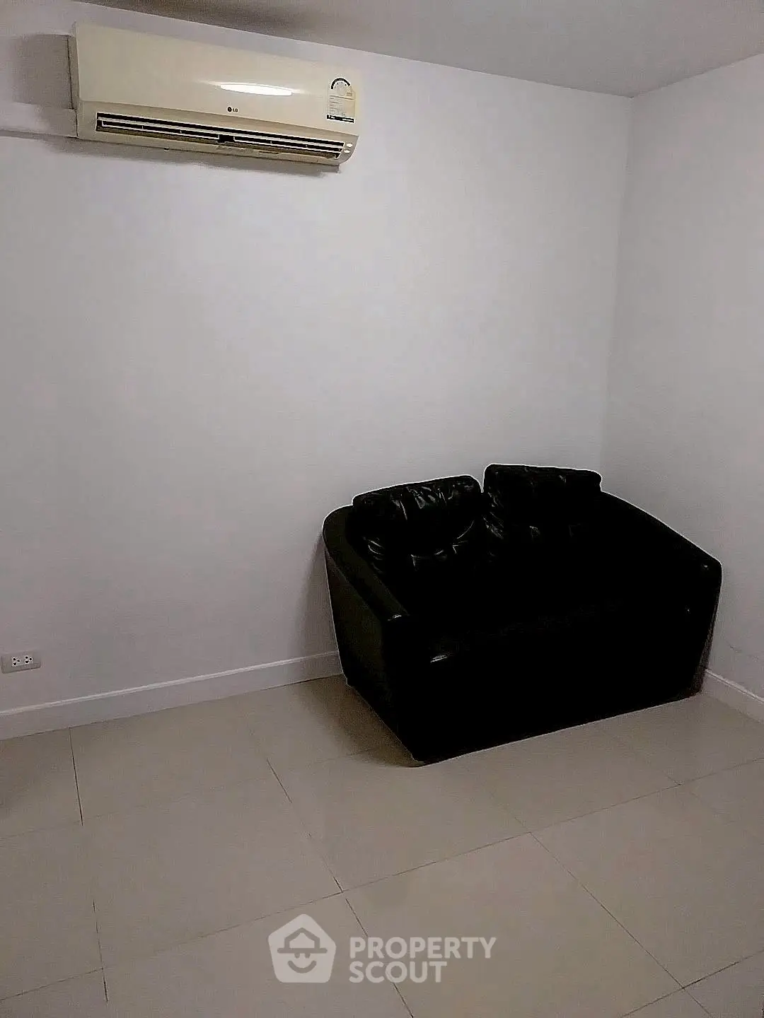 Minimalist room with black leather sofa and wall-mounted air conditioner.