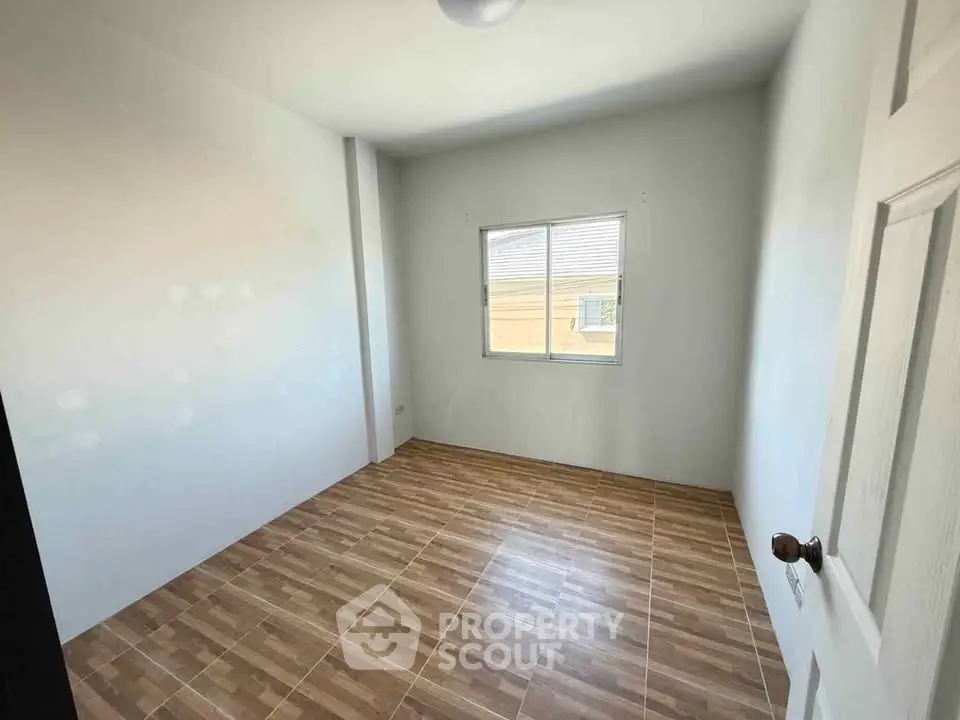 Spacious empty bedroom with wooden flooring and natural light.