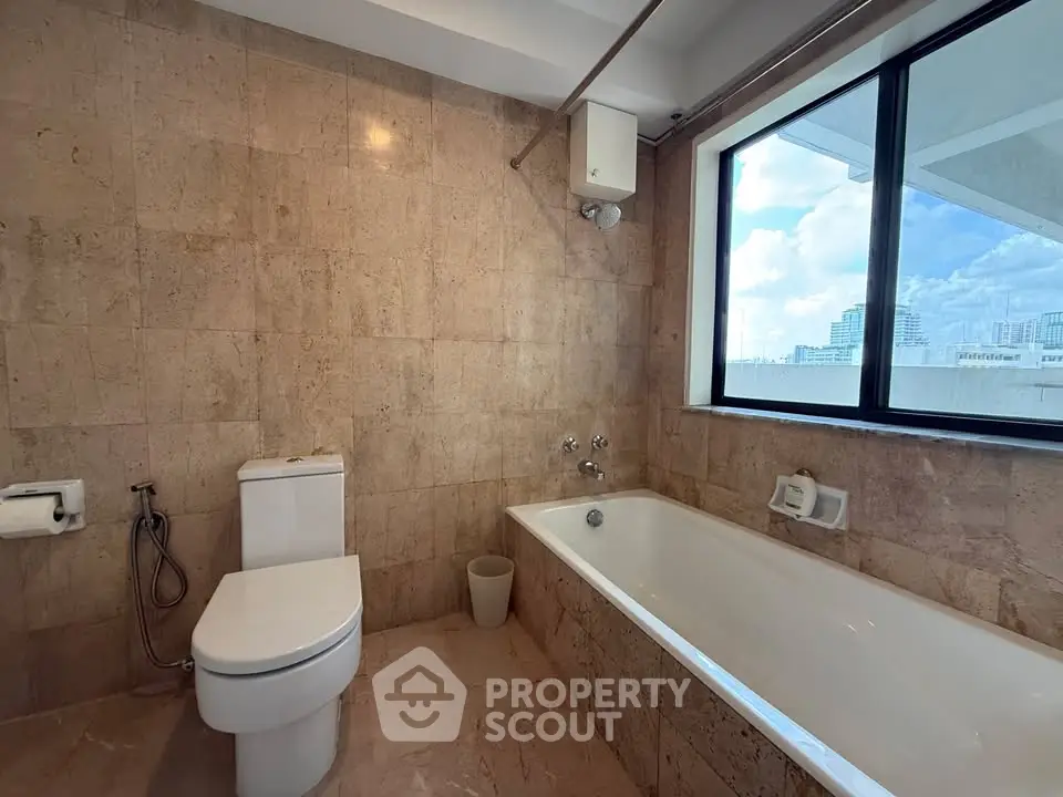 Spacious bathroom with bathtub and city view, featuring elegant stone tiles and large window.