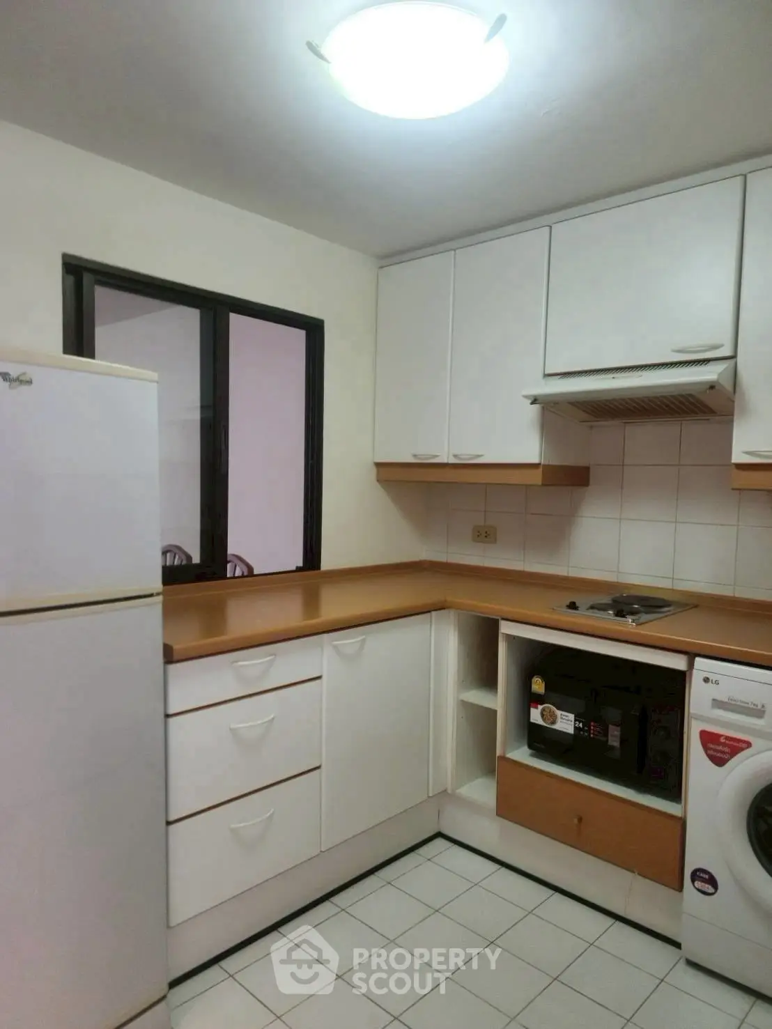Modern kitchen with white cabinets, fridge, and washing machine in cozy apartment.