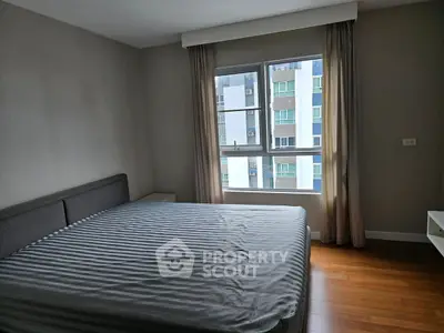 Spacious bedroom with large window and modern decor in urban apartment.