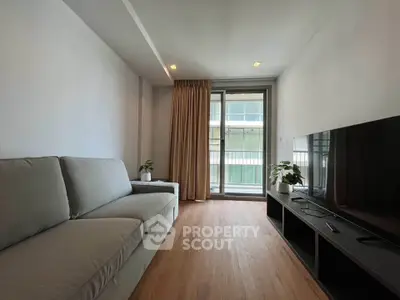 Modern living room with large sofa and flat-screen TV, featuring floor-to-ceiling windows and wooden flooring.