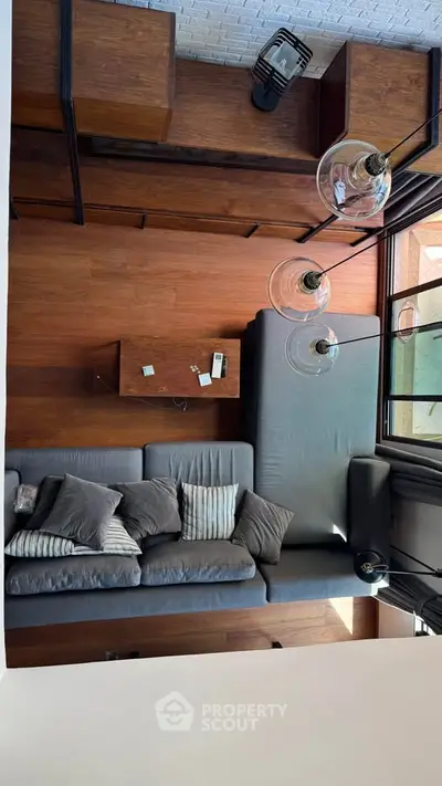 Modern living room with stylish gray sofa and wooden flooring, featuring large windows and elegant lighting.