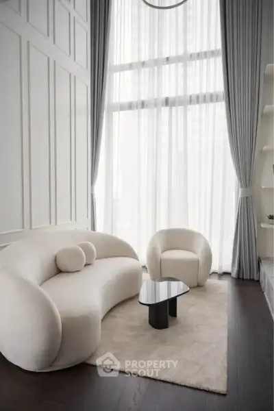 Elegant living room with modern furniture and floor-to-ceiling windows, featuring a stylish sofa and armchair.