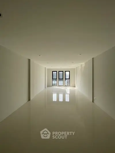 Spacious empty room with glossy floors and large windows, perfect for customization.