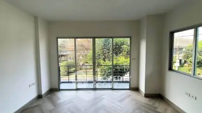 Spacious room with large windows and balcony overlooking lush greenery, perfect for serene living.