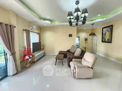 Spacious living room with modern decor and natural light, featuring a cozy seating area and elegant chandelier.