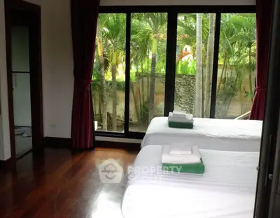 Spacious bedroom with large windows offering lush garden views, featuring twin beds and elegant wooden flooring.