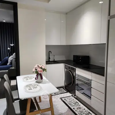 Modern kitchen with sleek white cabinets, built-in oven, and washing machine, adjacent to cozy dining area.