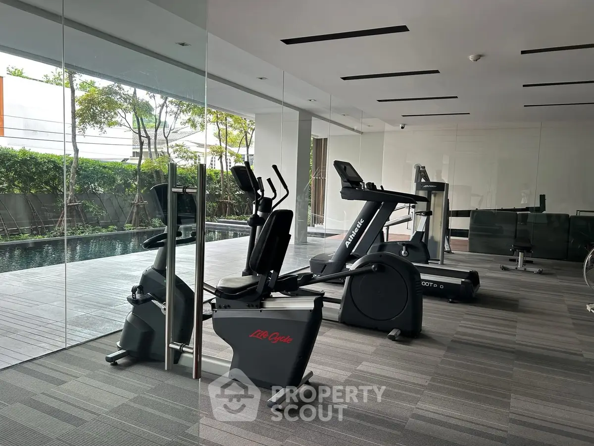 Modern gym with state-of-the-art equipment and pool view in luxury apartment complex.