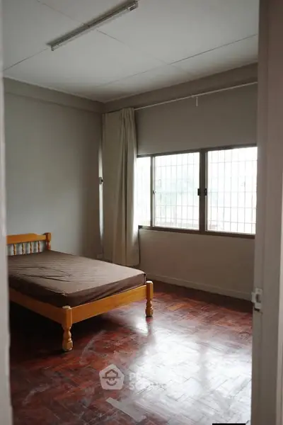 Spacious bedroom with wooden flooring and large windows for natural light.