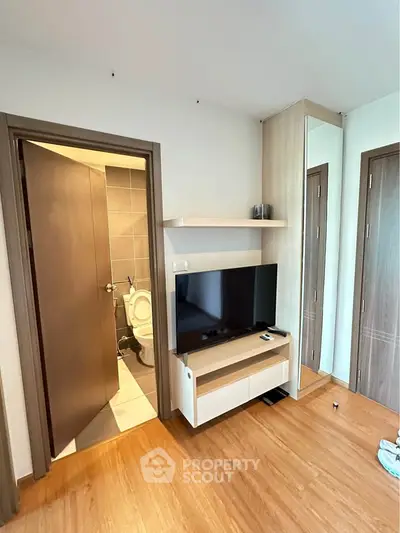 Modern living room with TV unit and wooden flooring, adjacent to a bathroom.