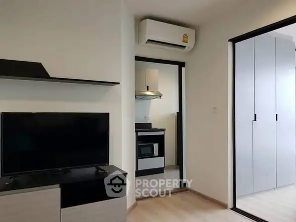 Modern apartment interior with sleek design, featuring a TV unit, air conditioning, and a compact kitchen area.