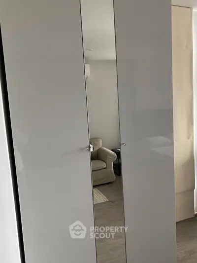 Modern bedroom with sleek mirrored wardrobe and cozy armchair.
