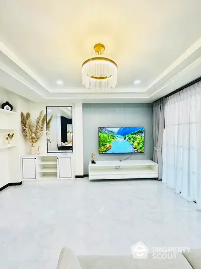 Luxurious modern living room with elegant chandelier, large flat-screen TV, and chic white decor, perfect for sophisticated living.