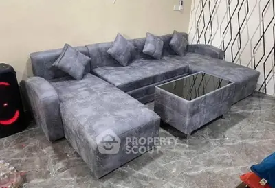 Modern living room with stylish gray sectional sofa and sleek glass-top coffee table on marble flooring.