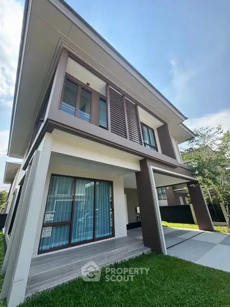 Modern two-story house with large windows and lush green lawn.