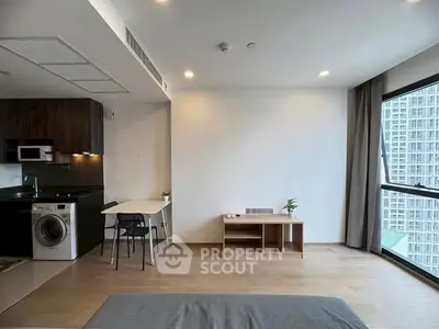 Modern studio apartment with open kitchen and large windows in urban setting.