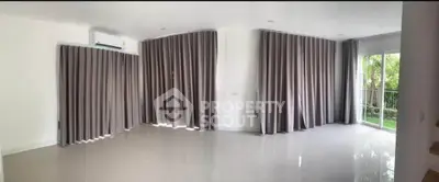Spacious living room with large windows and elegant curtains, offering a serene garden view.