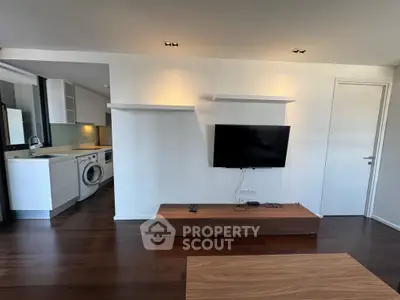 Modern living room with wall-mounted TV and open kitchen featuring washing machine.