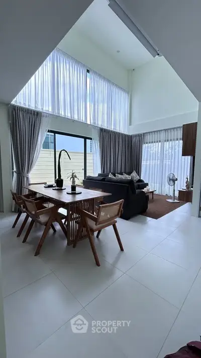 Spacious modern living room with high ceilings and large windows, featuring elegant dining area and cozy seating.