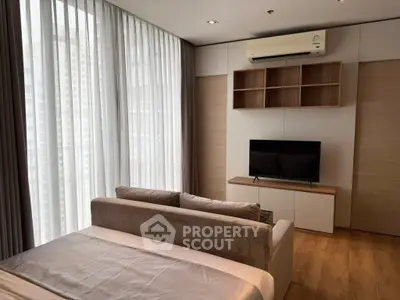 Modern bedroom with large windows, stylish TV setup, and cozy sofa in a high-rise apartment.