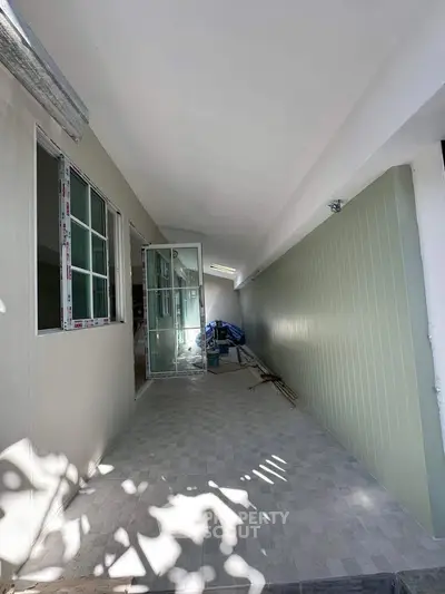 Spacious corridor with modern glass door and tiled flooring, ideal for versatile use in any property.