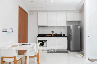 Modern kitchen with sleek white cabinets and stainless steel fridge in a cozy apartment.
