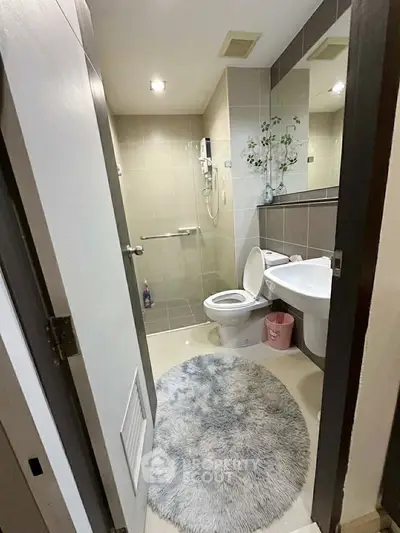 Modern bathroom with sleek fixtures and stylish decor, featuring a round plush rug and contemporary shower area.