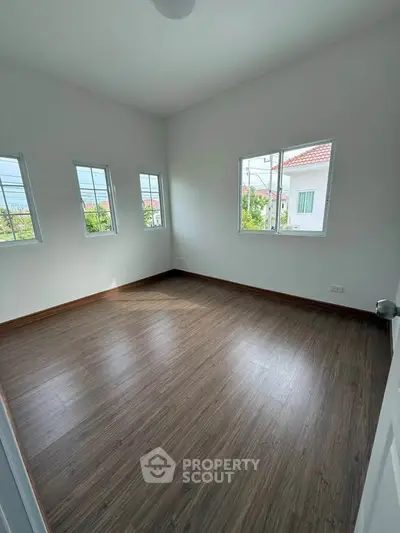 Spacious empty room with wooden flooring and large windows offering natural light and neighborhood views.