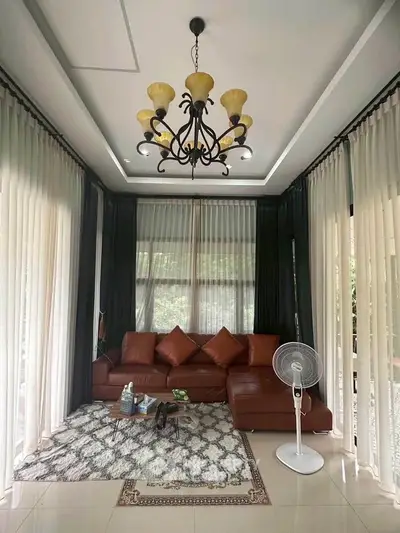 Elegant living room with leather sofa, chandelier, and large windows with curtains.