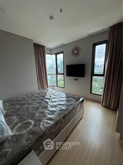 Modern bedroom with city view, featuring large windows and wall-mounted TV.