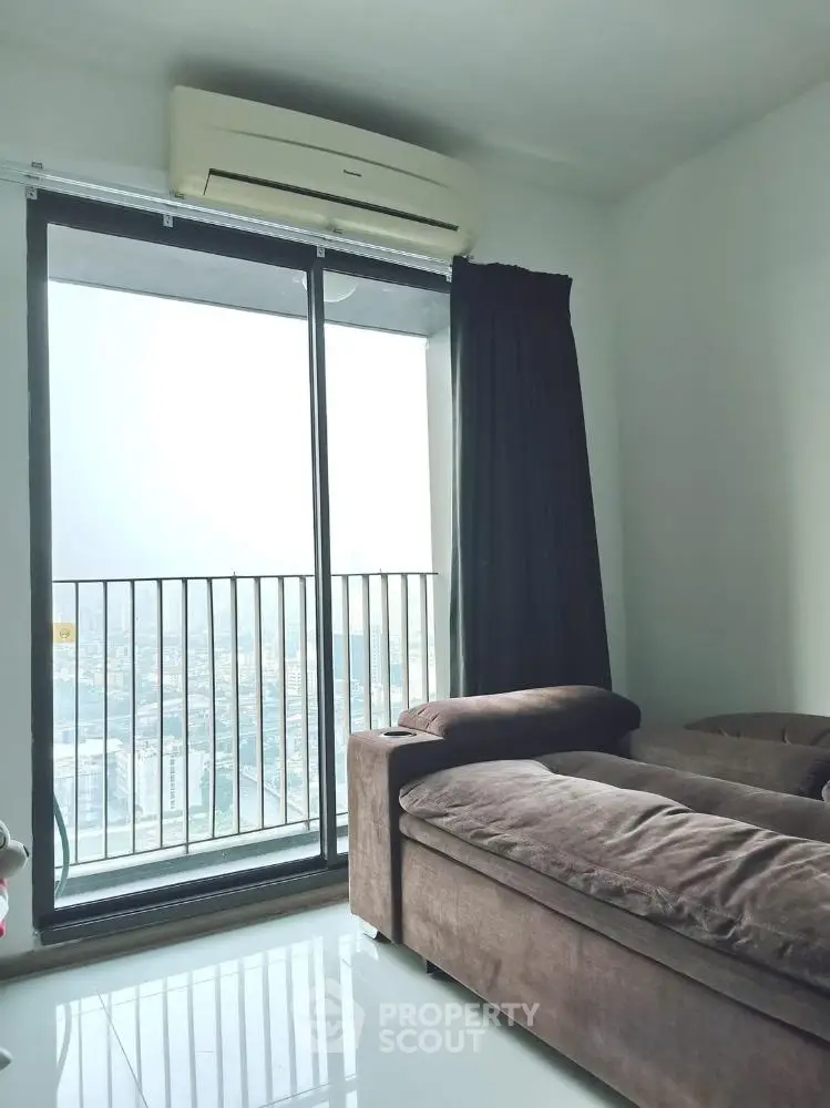 Modern living room with large window and city view, featuring a comfortable sofa and air conditioning.