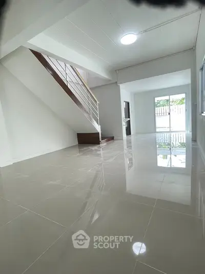 Spacious modern living room with glossy tiled floors and staircase, perfect for family gatherings.
