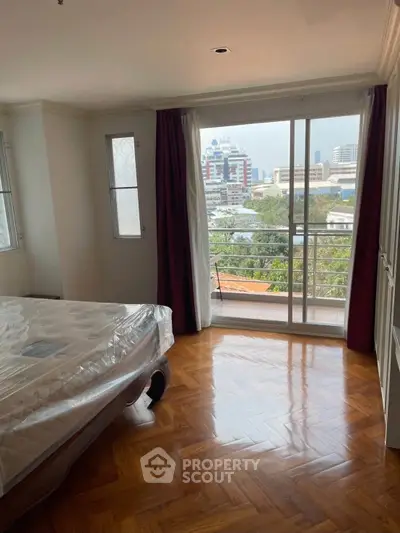 Spacious bedroom with large windows and city view, featuring elegant wooden flooring and natural light.