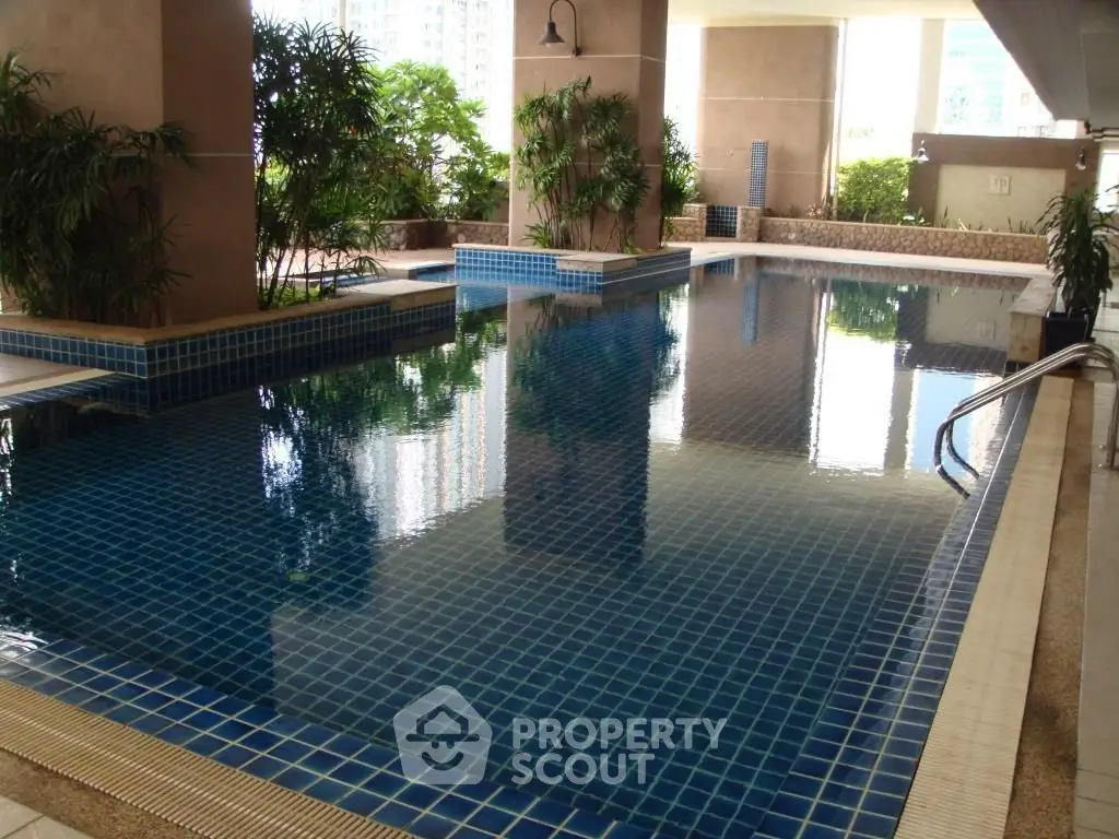 Luxurious indoor swimming pool with elegant blue tiles and lush greenery