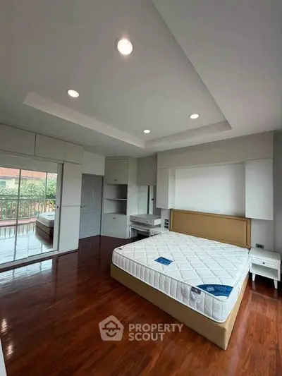 Spacious bedroom with hardwood floors and large windows overlooking greenery.