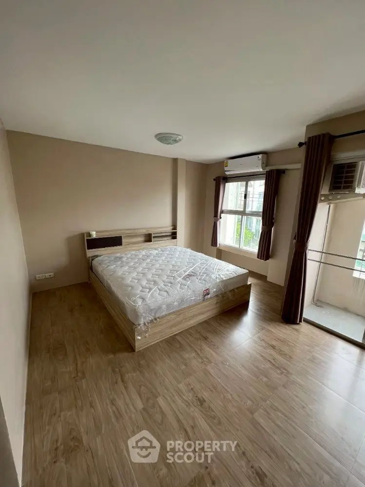 Spacious bedroom with wooden flooring and large windows in modern apartment.