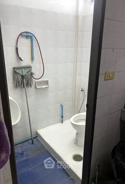 Compact bathroom with tiled walls and floor, featuring a toilet and cleaning supplies.