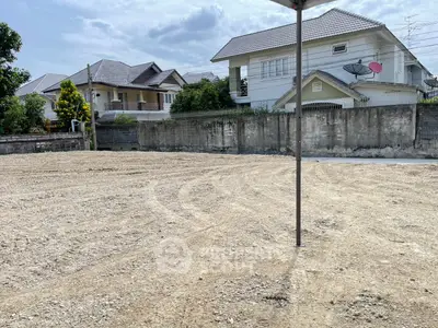 Vacant land plot in a residential area with nearby houses, ideal for new construction.